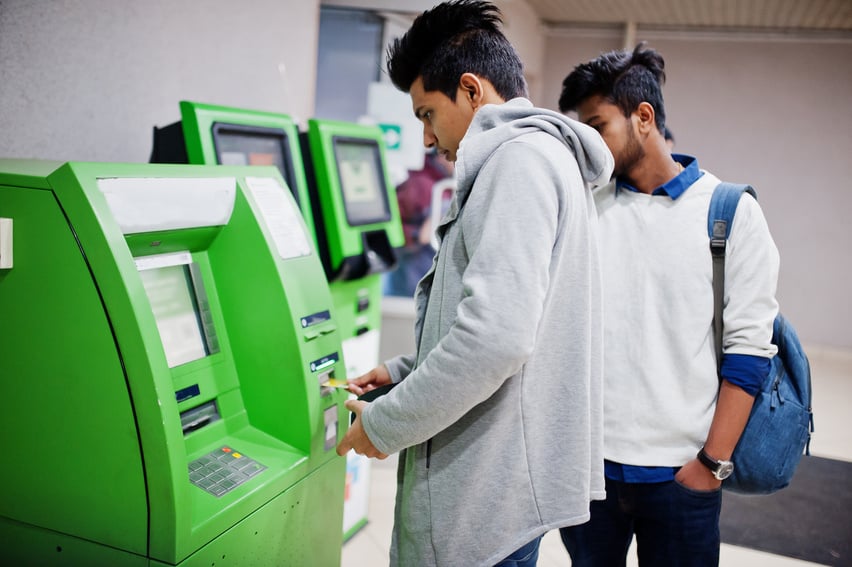 Two asian guys removes cash from an green ATM.